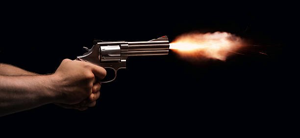 A revolver held by two anonymous hands is fired on a black background.